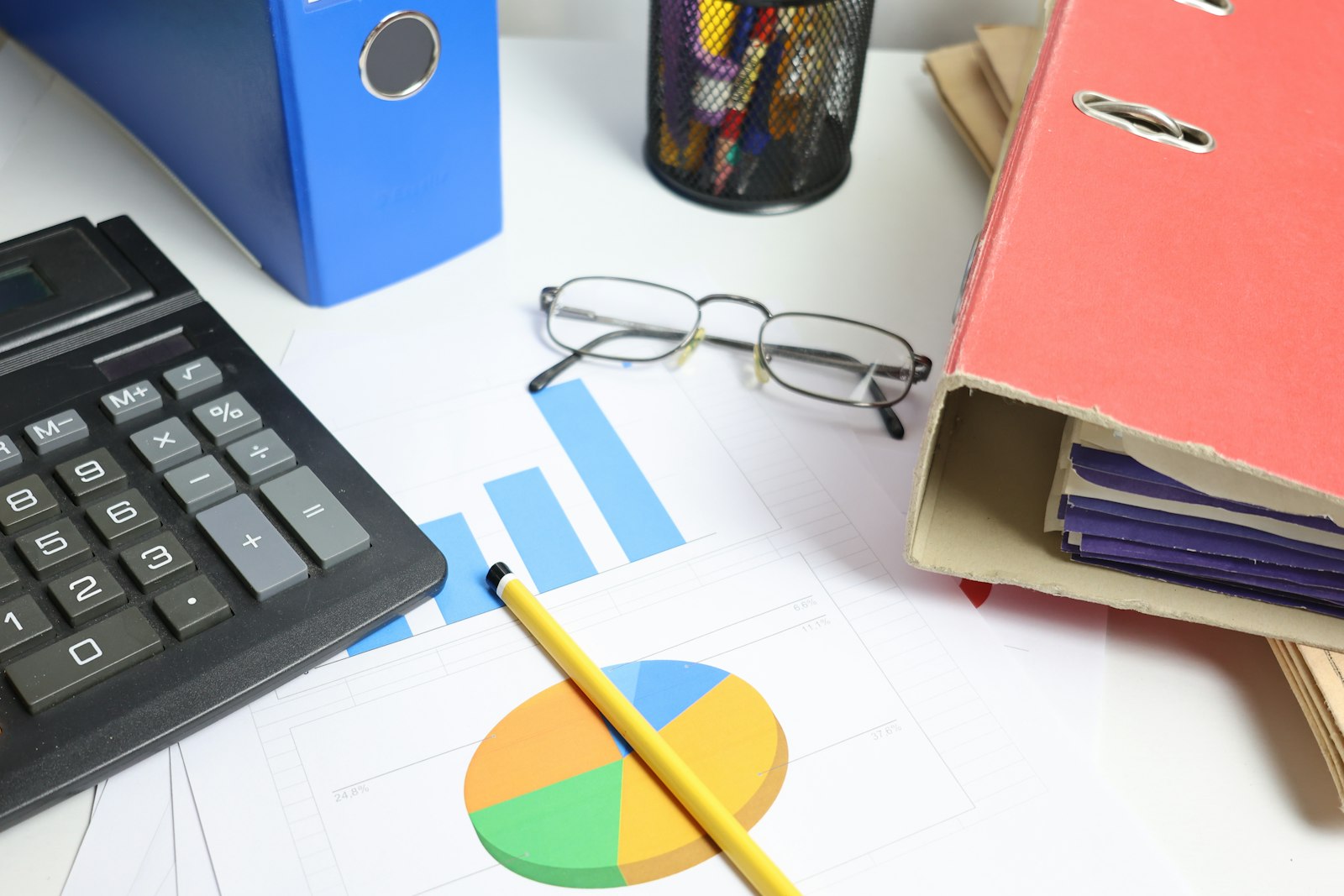 A desk with a calculator, printed charts and binders, representing the payback arithmetic that should sit behind an AI budget approval