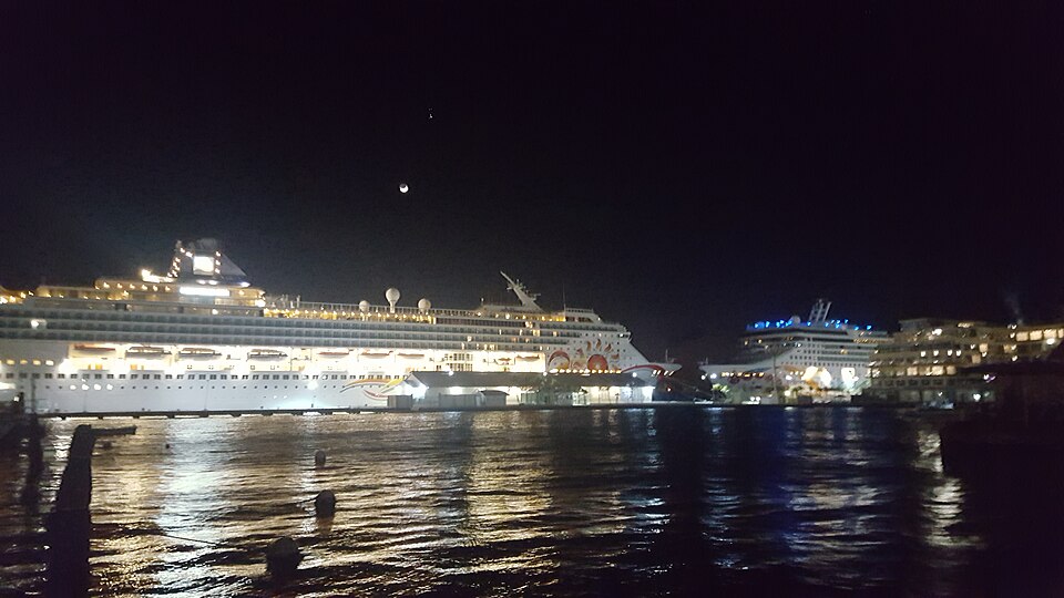 Two cruise ships docked at night in the harbour at Oranjestad, Aruba, their lights reflected in the water