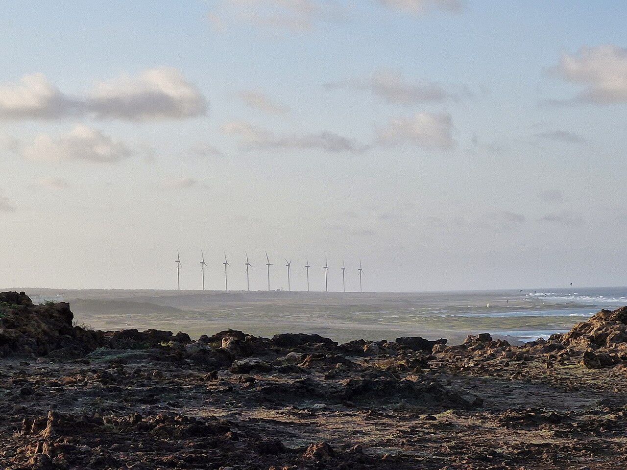Vader Piet wind turbines on the horizon beyond the rocky limestone coast near San Nicolas, Aruba