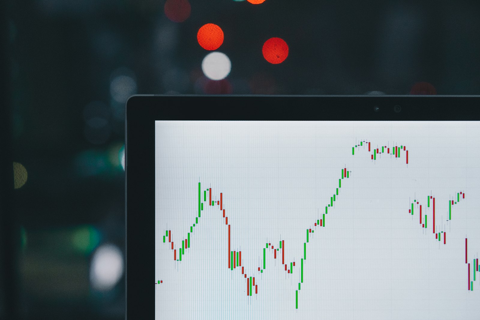 A laptop displaying a candlestick chart at night, representing the conventional tabular and charting interface most retail investors first encounter