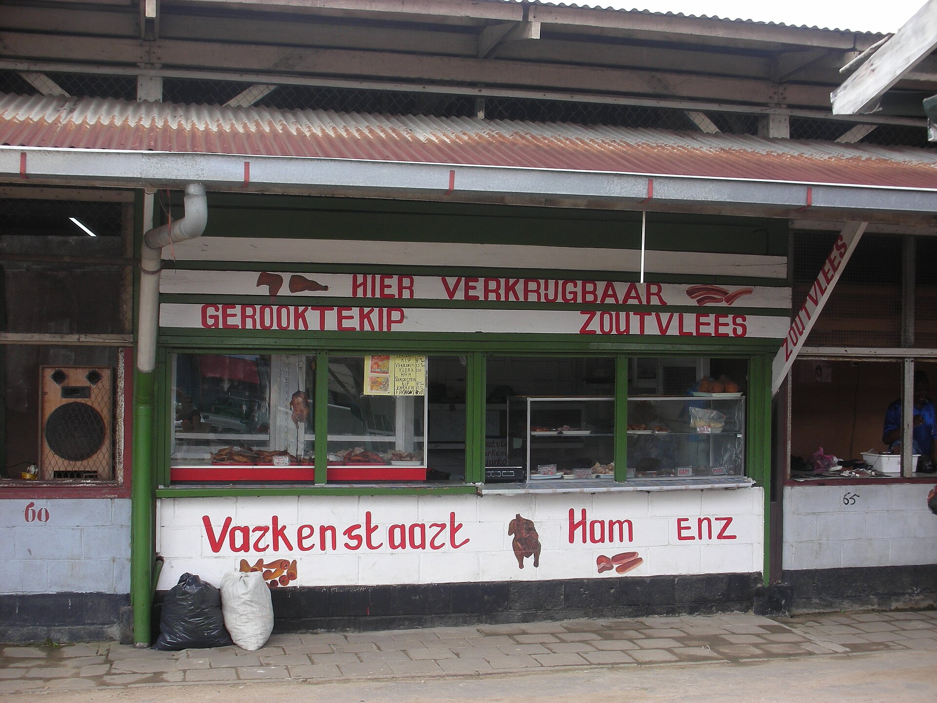 Meat stall in a Paramaribo market selling smoked chicken, salted meat and ham, with hand-painted Dutch signs